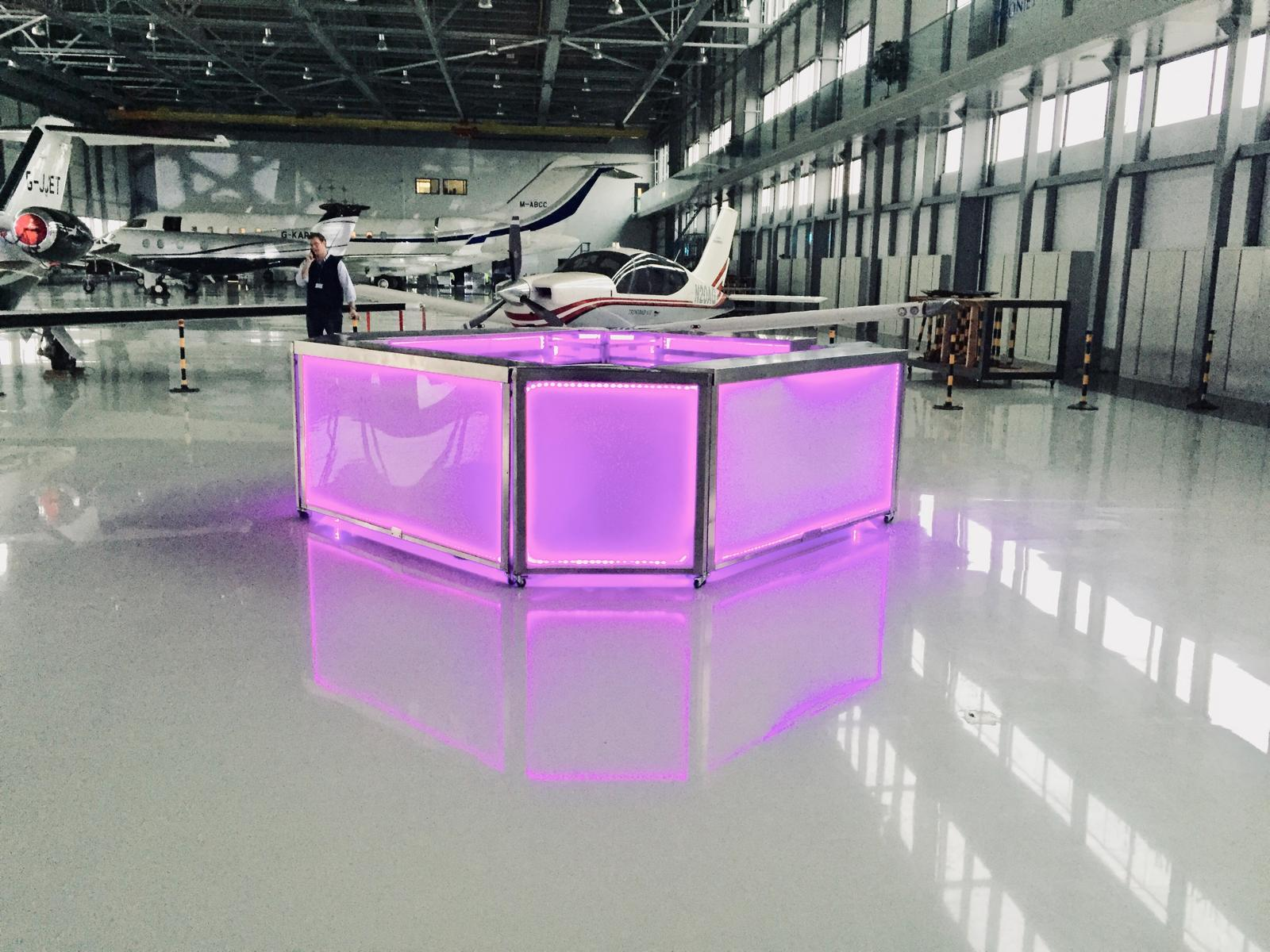 Purple-lit island mobile bar installed inside a private jet hangar corporate event space