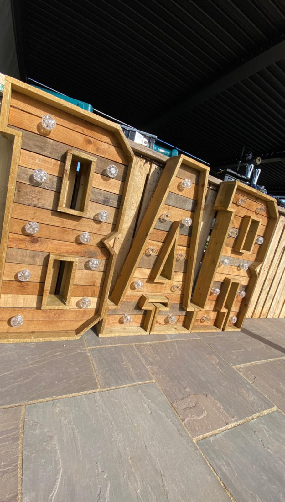 Large rustic reclaimed wood BAR letters with vintage bulbs set up on a patio