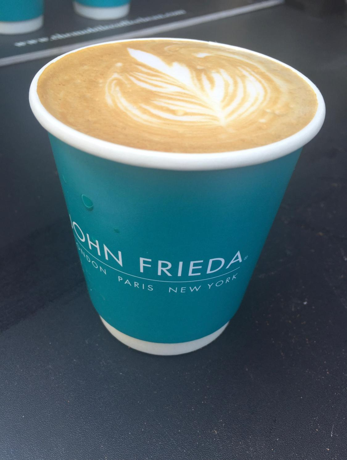 Close-up of a John Frieda branded takeaway coffee cup with latte art on top