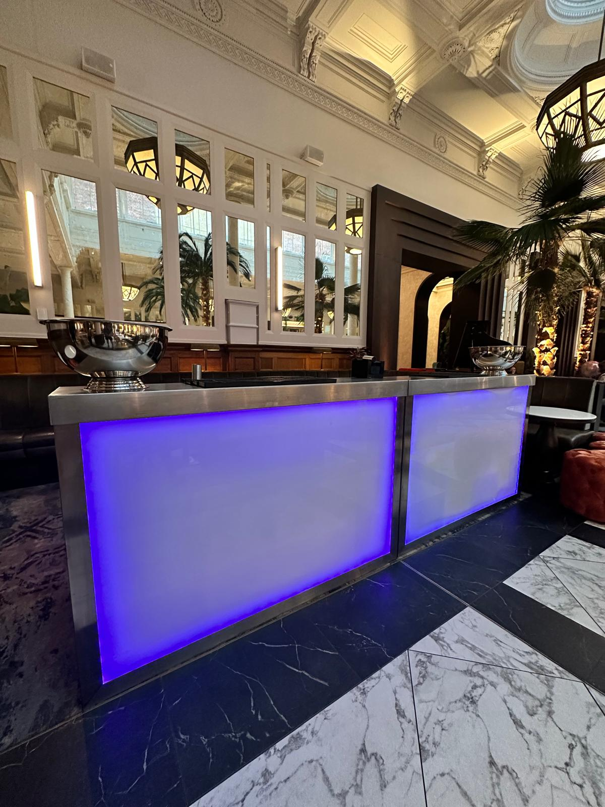 Blue-lit modular mobile bar installed inside The Municipal hotel with marble floors and palm-lined interiors