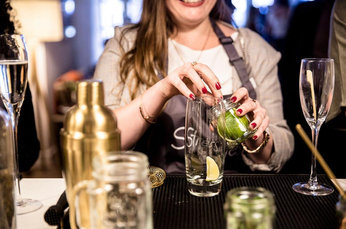 Guest in a Stressless branded apron dropping a fresh lime wedge into a highball glass at a cocktail masterclass