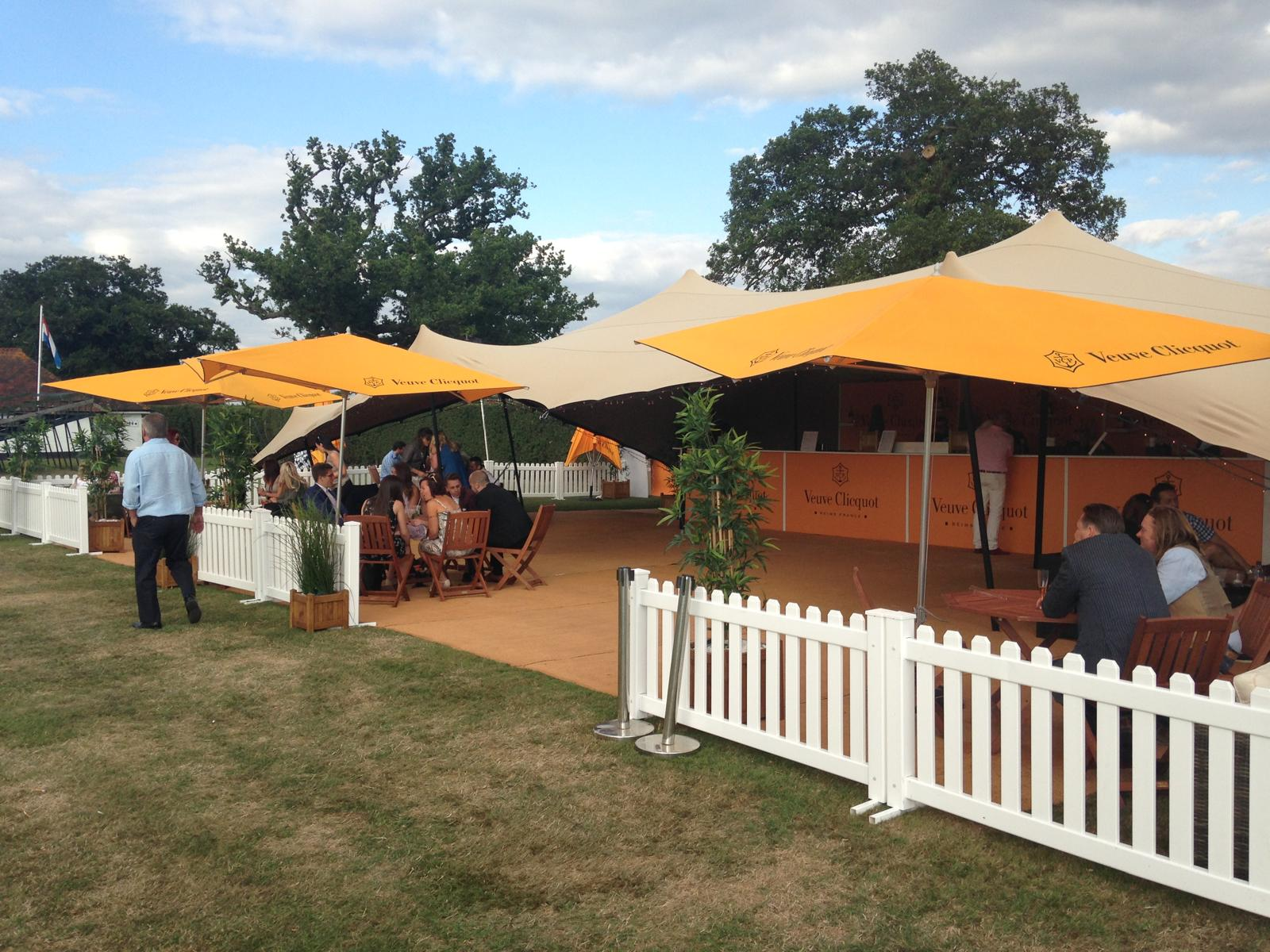 Guests dining under Veuve Clicquot orange parasols and stretch tent at an outdoor festival hospitality bar
