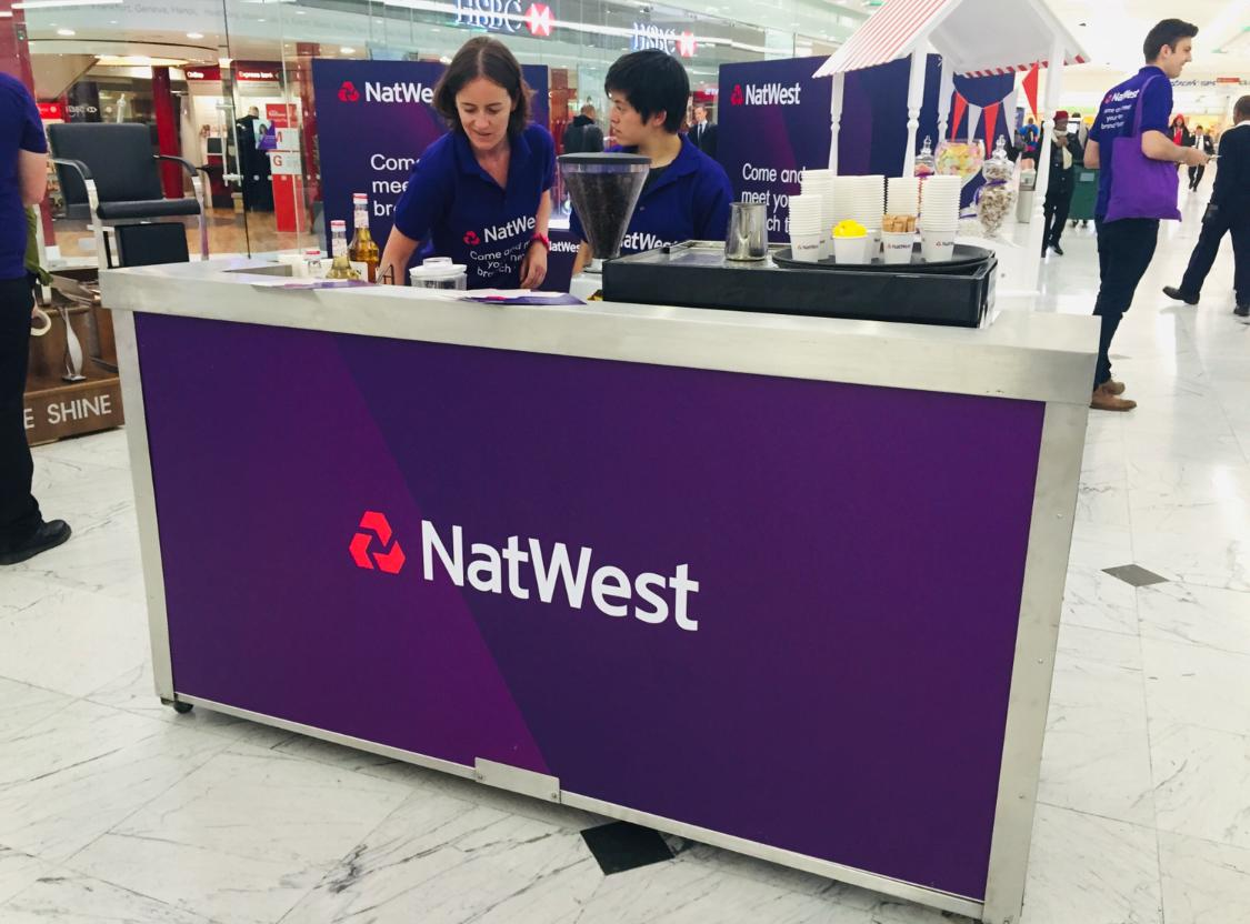 Close-up of a NatWest branded mobile coffee bar with cups, grinder and activation staff behind the counter