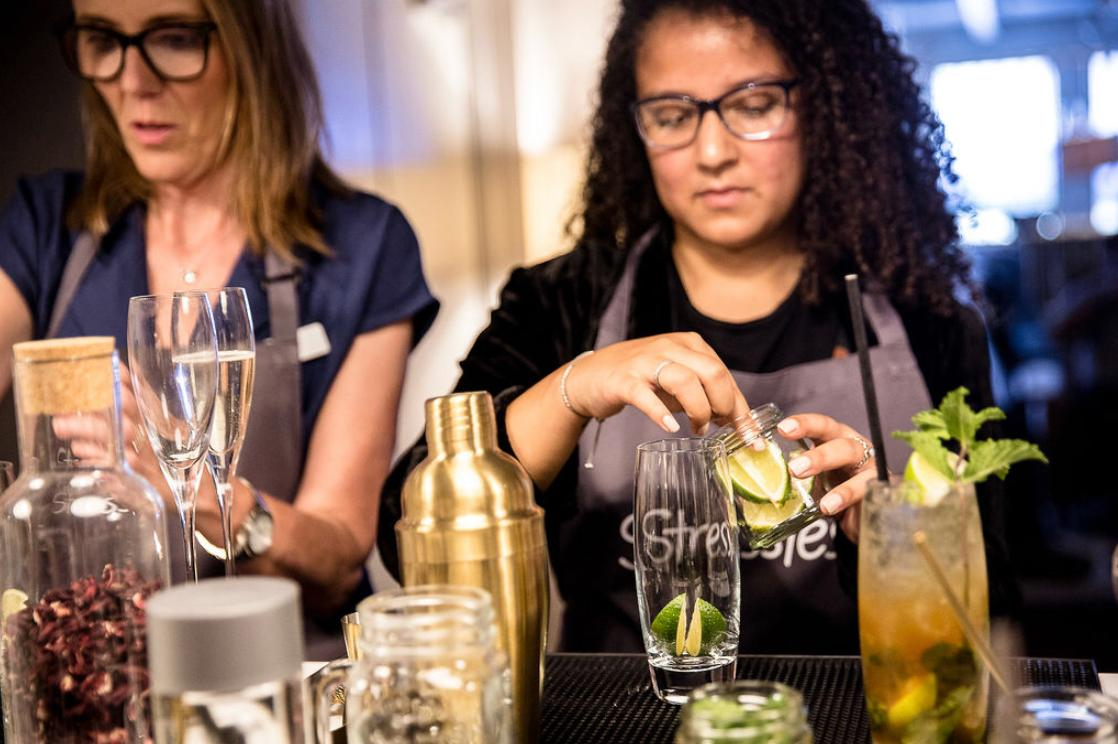 Two guests in Stressless branded aprons building mojitos with limes and mint at a hands-on cocktail masterclass