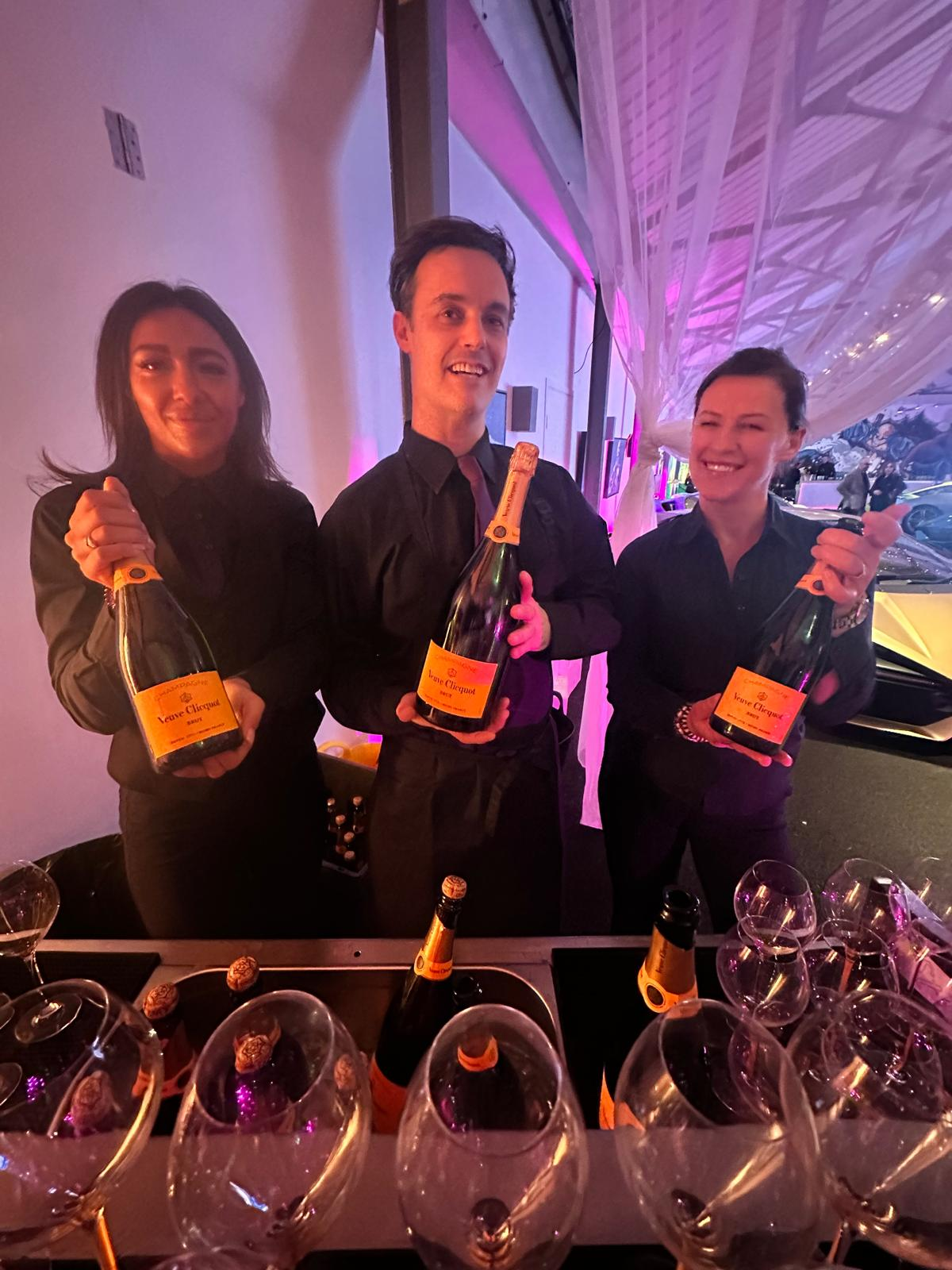 Champagne service team holding Veuve Clicquot bottles behind the bar