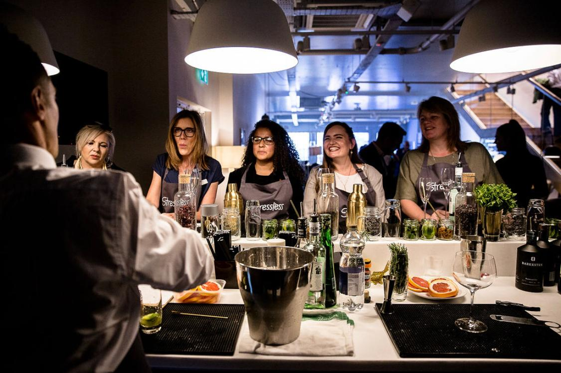 Guests gathered around a cocktail masterclass bar listening to the tutor during a live session