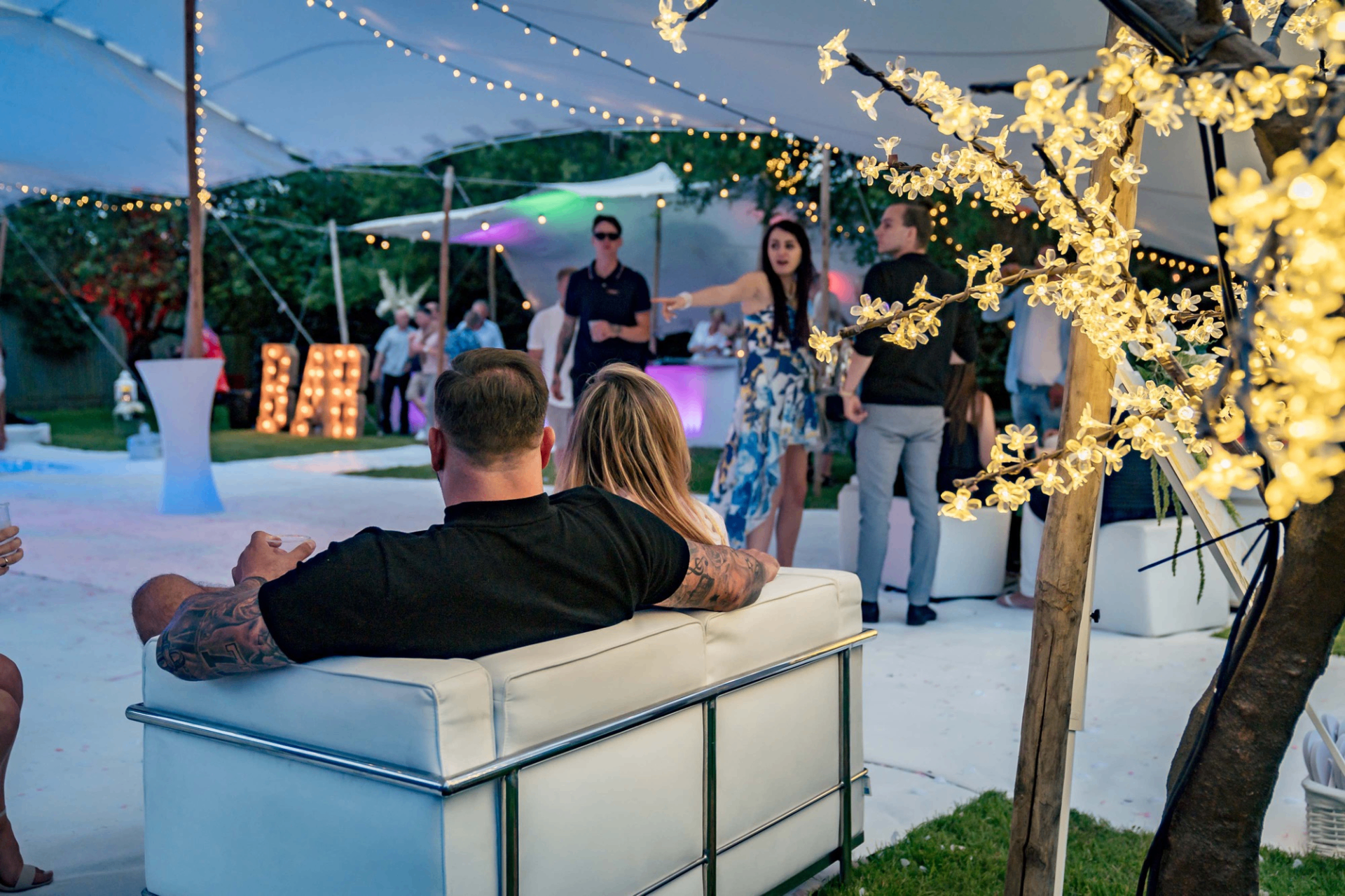 Guests relaxing under festoon and blossom lights at an evening wedding reception