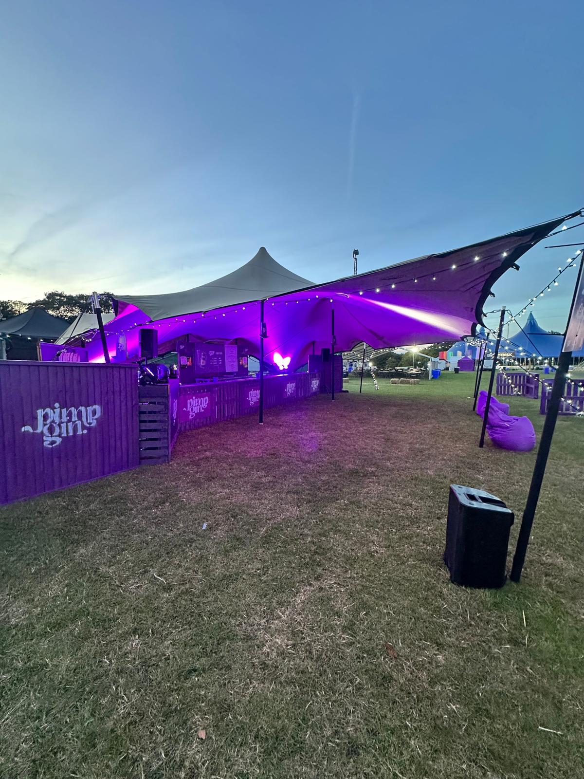 Pink Pony Gin festival bar lit up at dusk inside a stretch tent