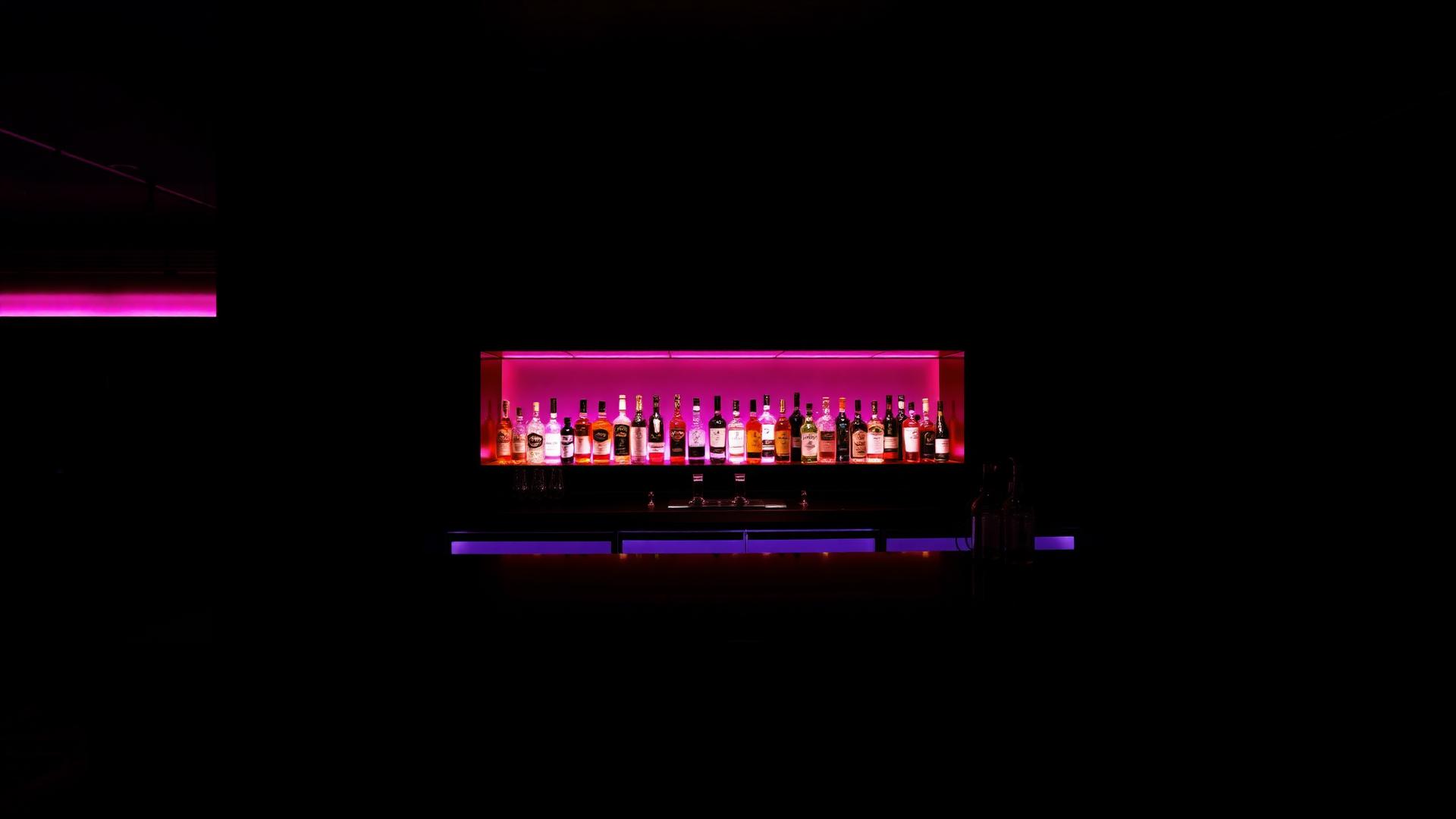 Sleek black corporate event bar with subtle magenta-lit back-bar bottles